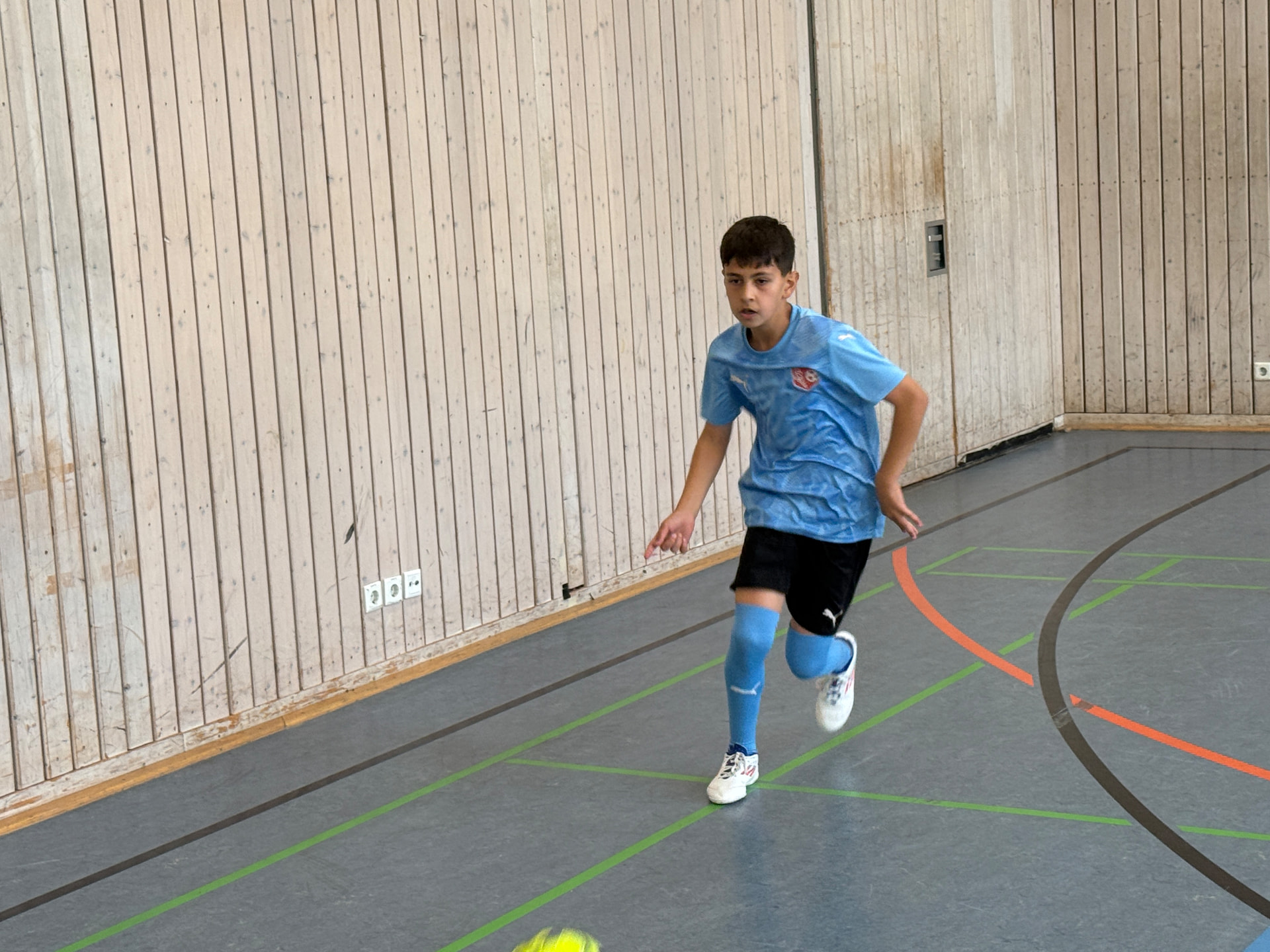 Junge im hellblauen Trikot sprintet in der Sporthalle einem Ball entgegen