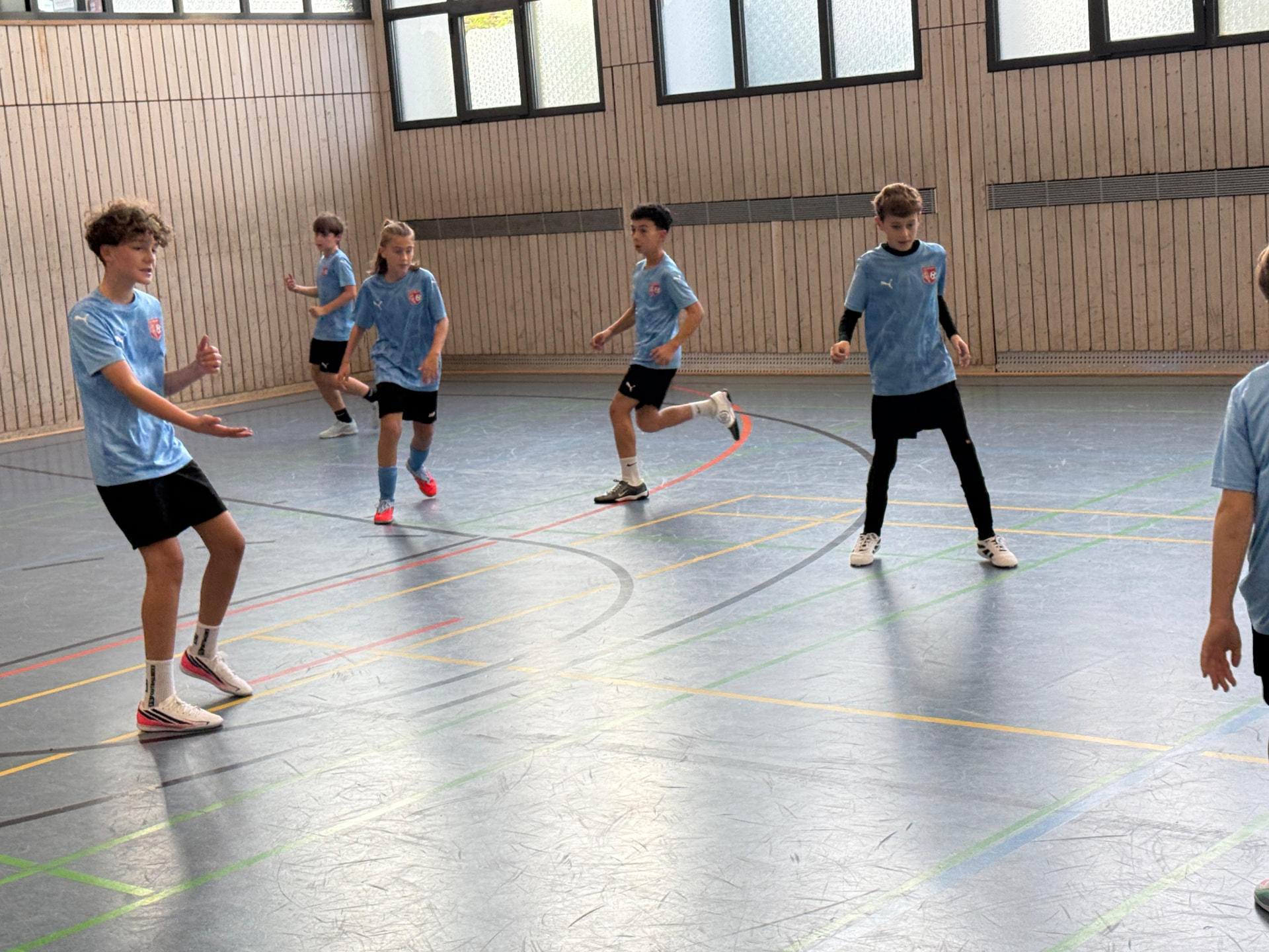 Mehrere Kinder im hellblauen Trikot beim Fußballspiel in der Sporthalle