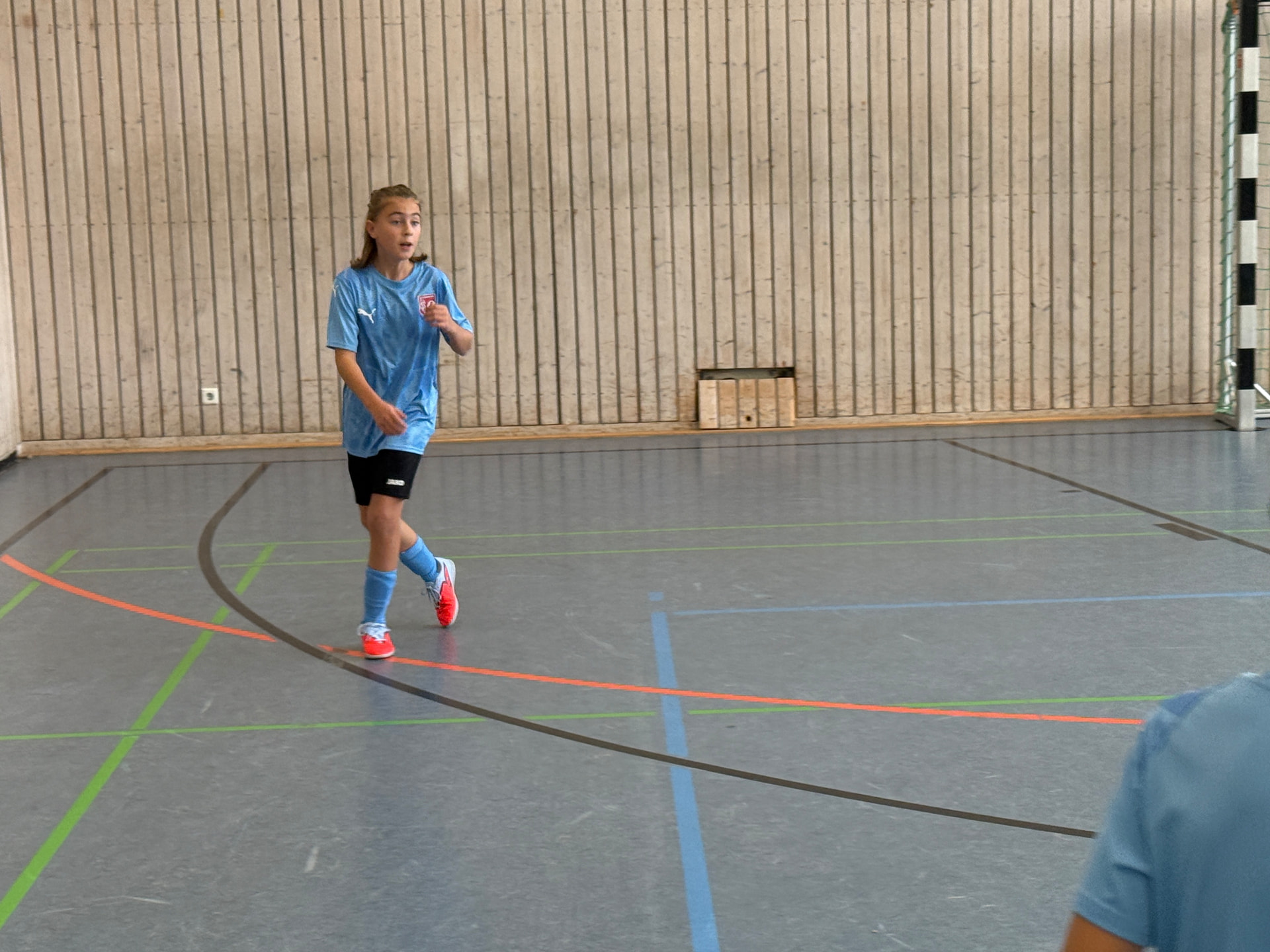 Kind im hellblauen Trikot läuft in der Sporthalle über das Spielfeld